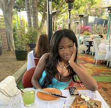 a young woman rests her cheek on her palm across a table